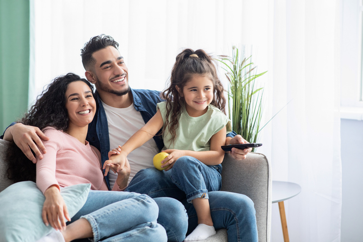 Three people on a couch with the man holding a TV remote